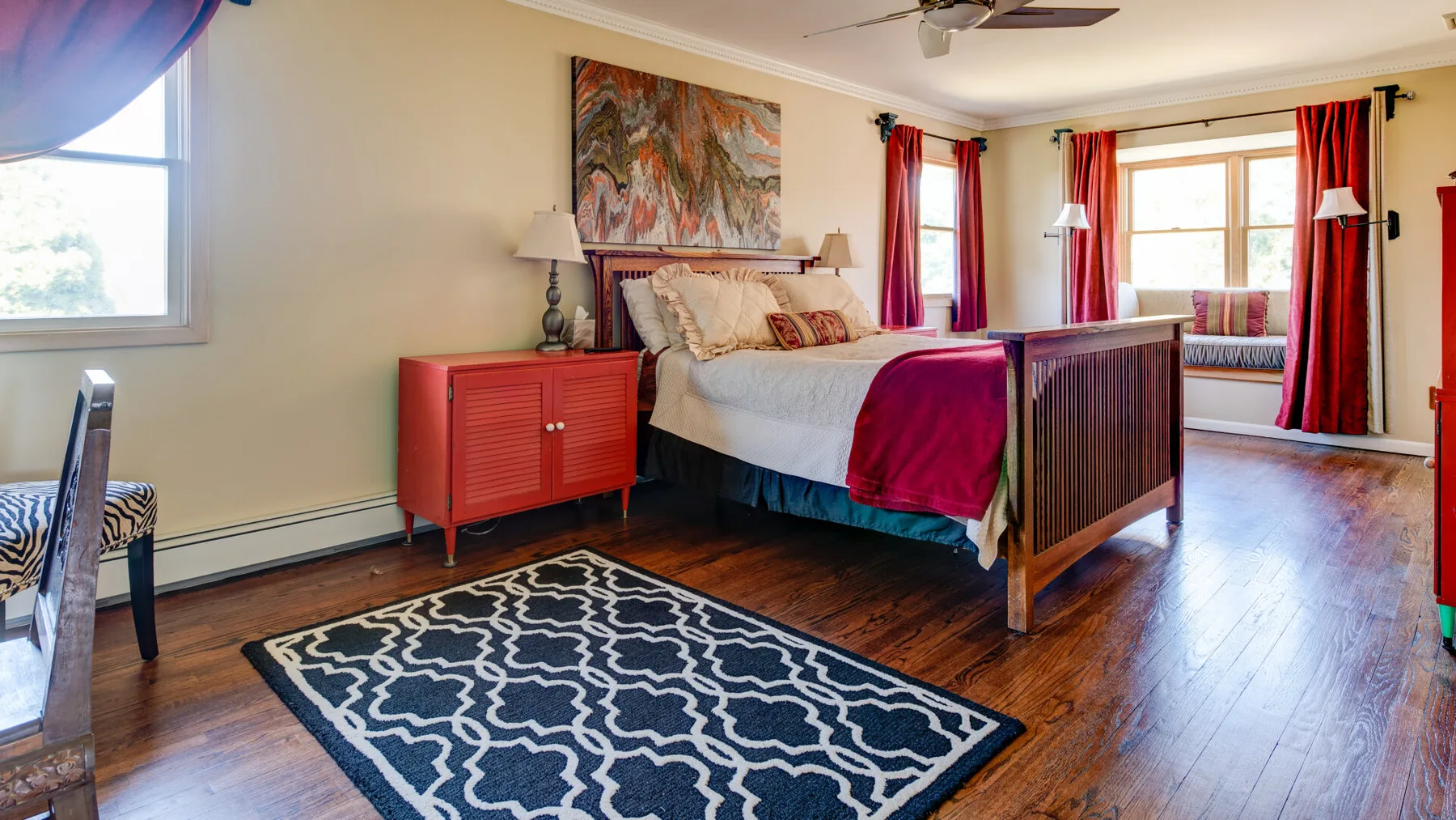 Un dormitorio con una cama grande, cortinas rojas y una alfombra estampada.