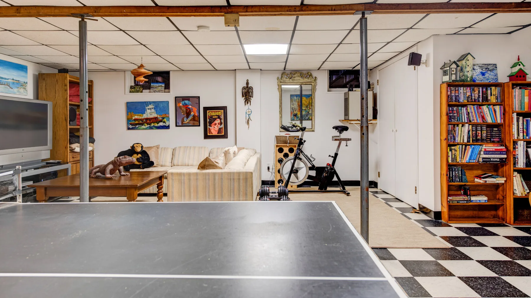 Una sala de recreación en el sótano con mesa de ping-pong, asientos y equipo de ejercicio.