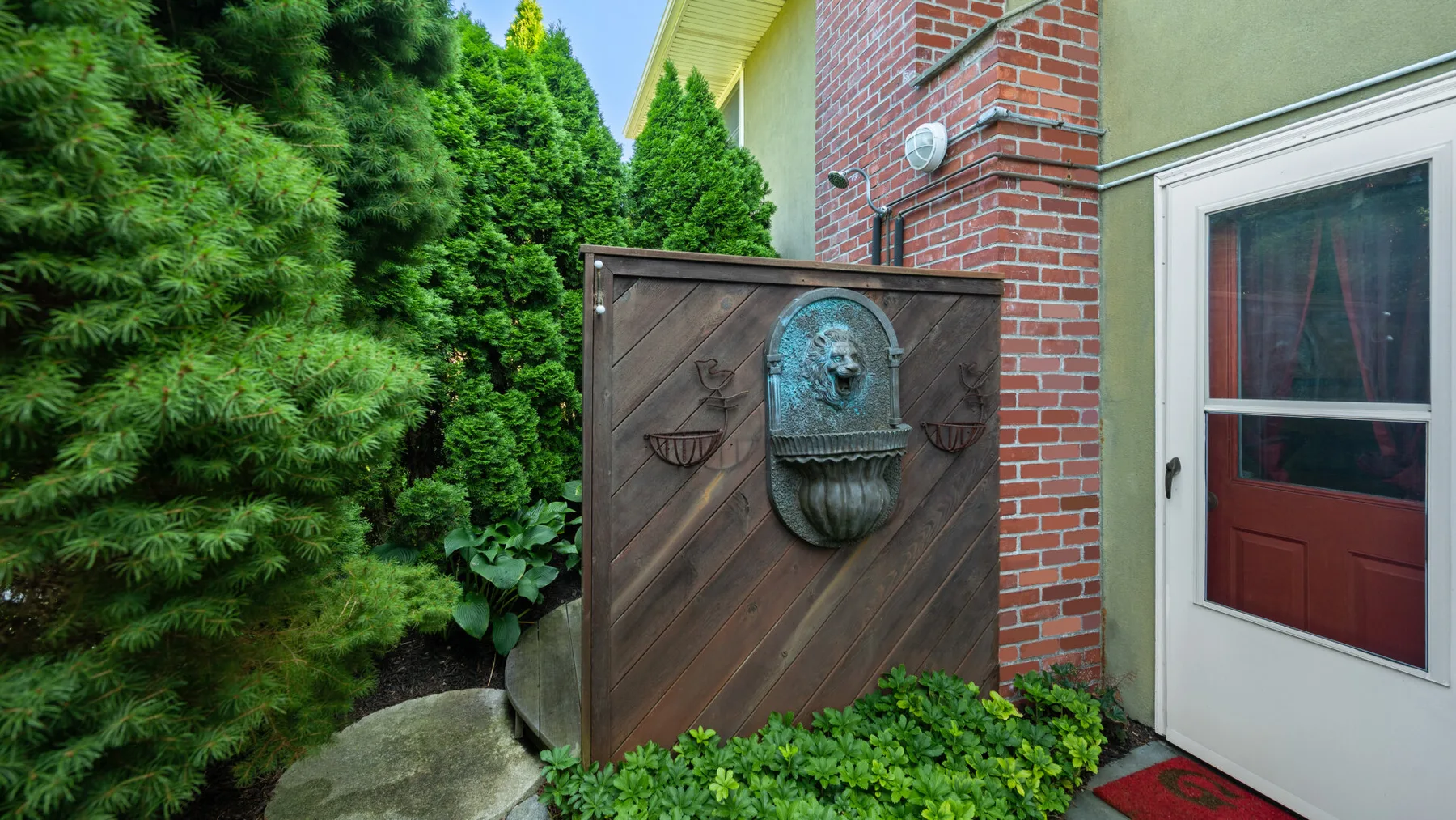 Entrada de una casa de ladrillo junto a una puerta de madera y vegetación frondosa.