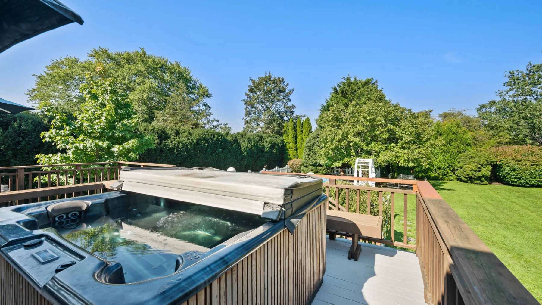 Un jacuzzi está en una terraza de madera con vistas a un jardín frondoso.