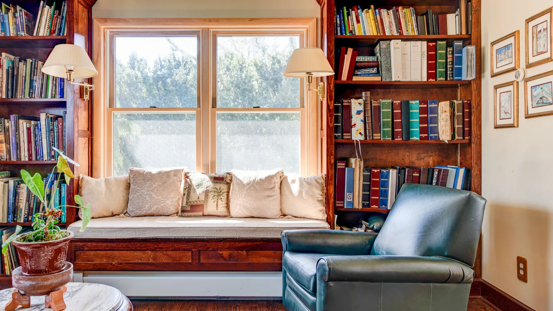 Un acogedor rincón de lectura con asiento junto a la ventana, estanterías y un sillón.