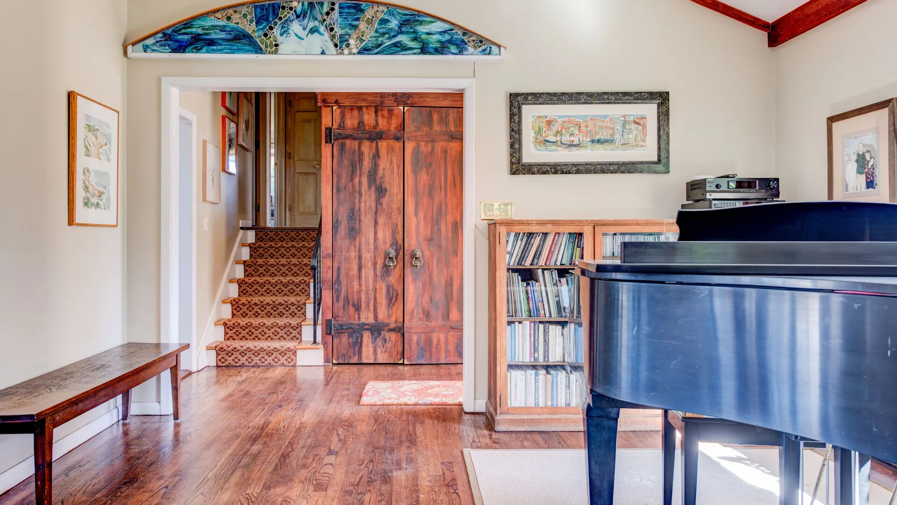 Una habitación con suelo de madera, un piano, una librería y una escalera.