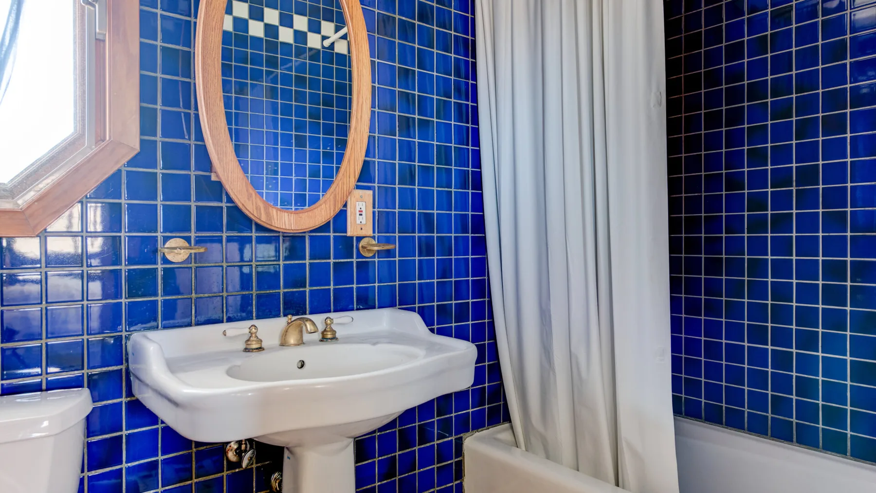 Un baño con un lavabo blanco y una cortina junto a paredes de azulejos azules.