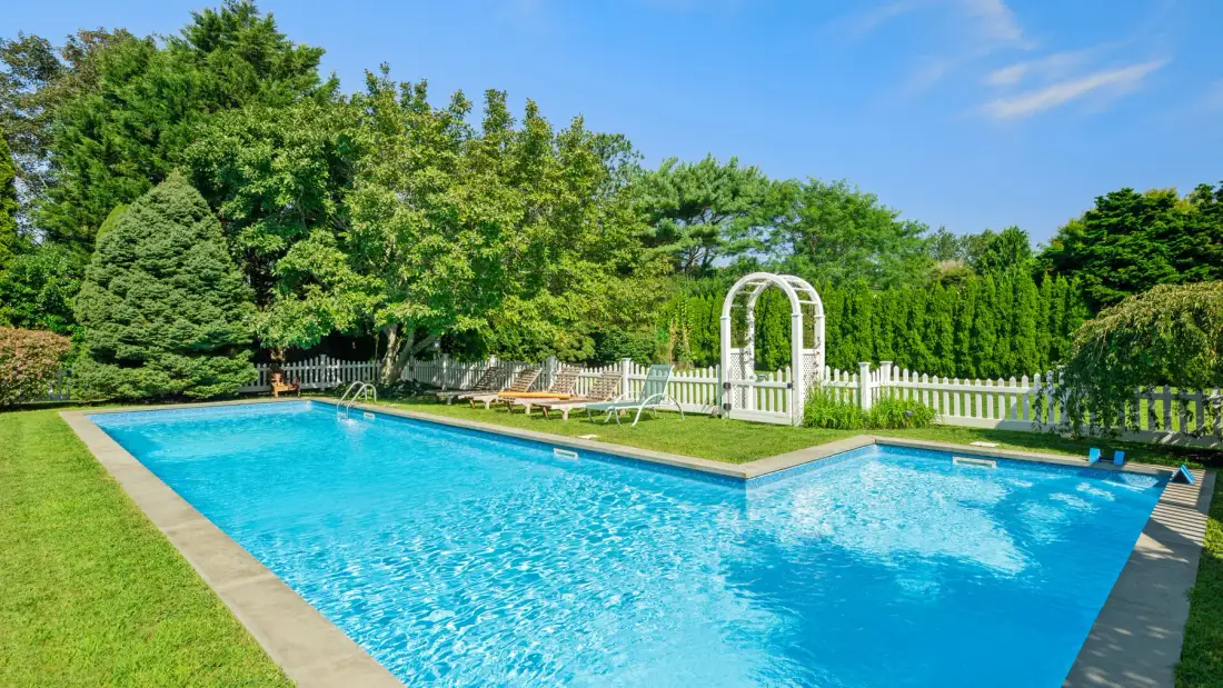 Una piscina al aire libre está junto a un arco de jardín blanco y árboles frondosos.