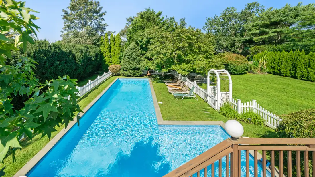 Una piscina está junto a un césped bien cuidado y un jardín frondoso.