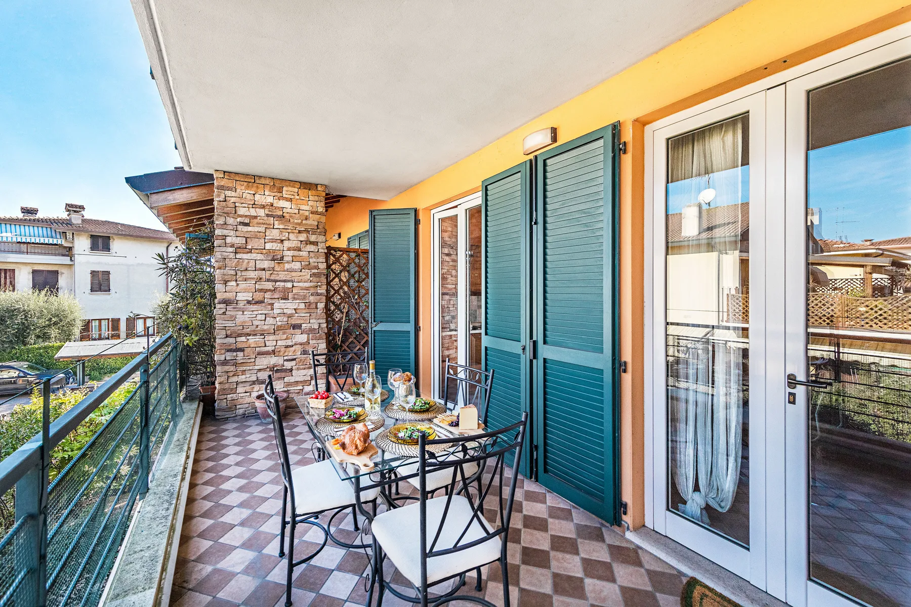 A balcony dining area with a table and chairs beside open teal shutters.