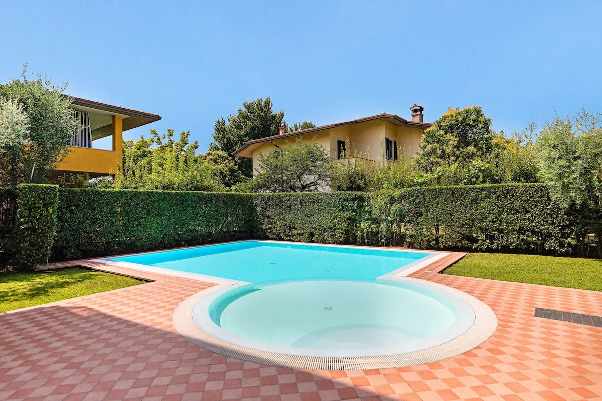 An outdoor swimming pool and circular shallow basin sit beside a tiled patio.