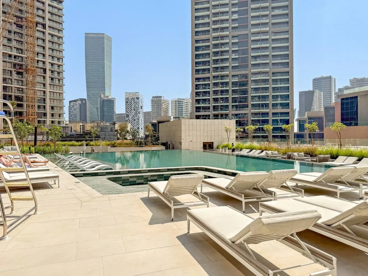 Una terraza con piscina y asientos de descanso, con edificios altos al fondo.