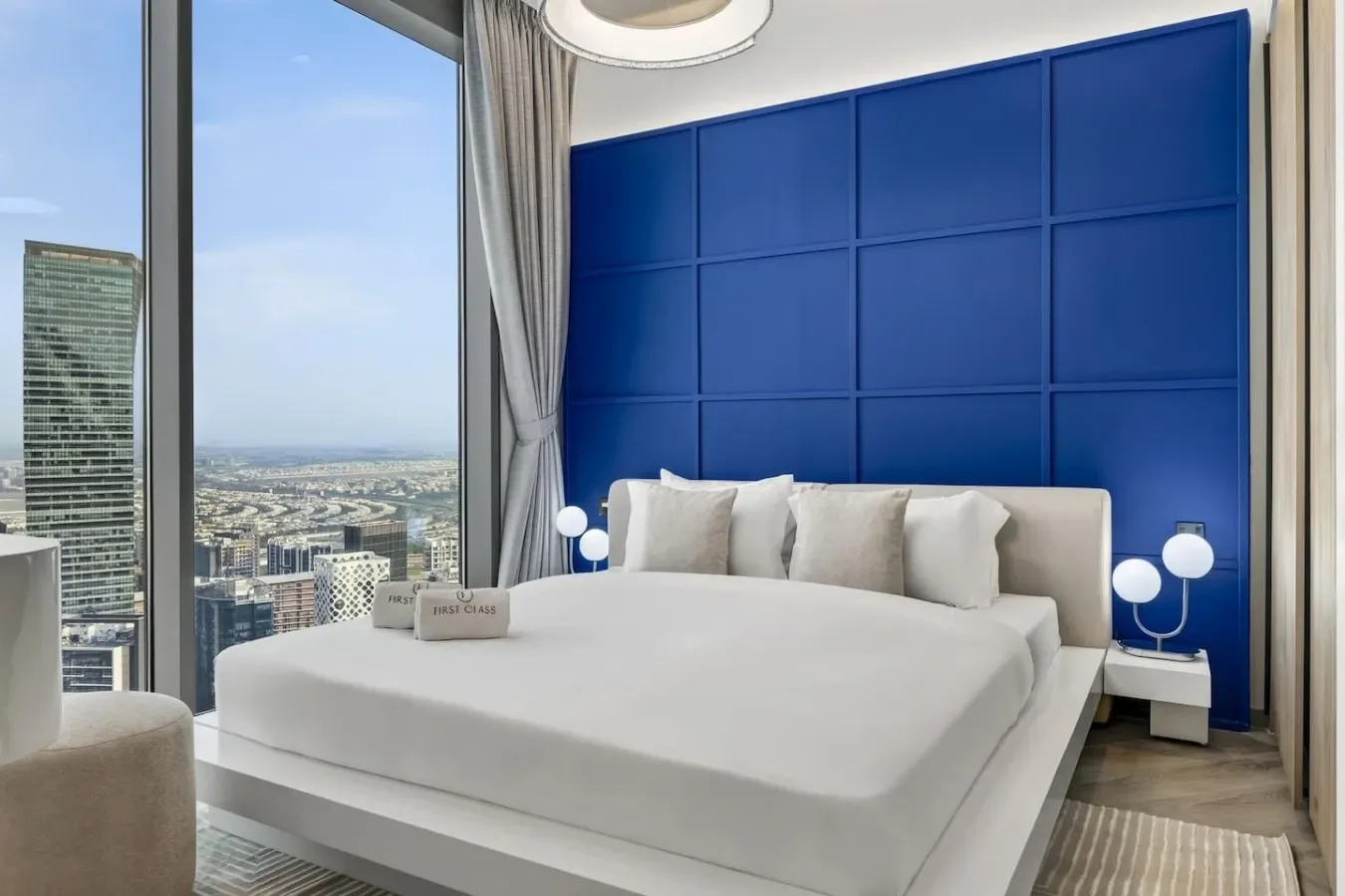 Dormitorio con una cama grande junto a una pared azul con paneles y ventanas altas.