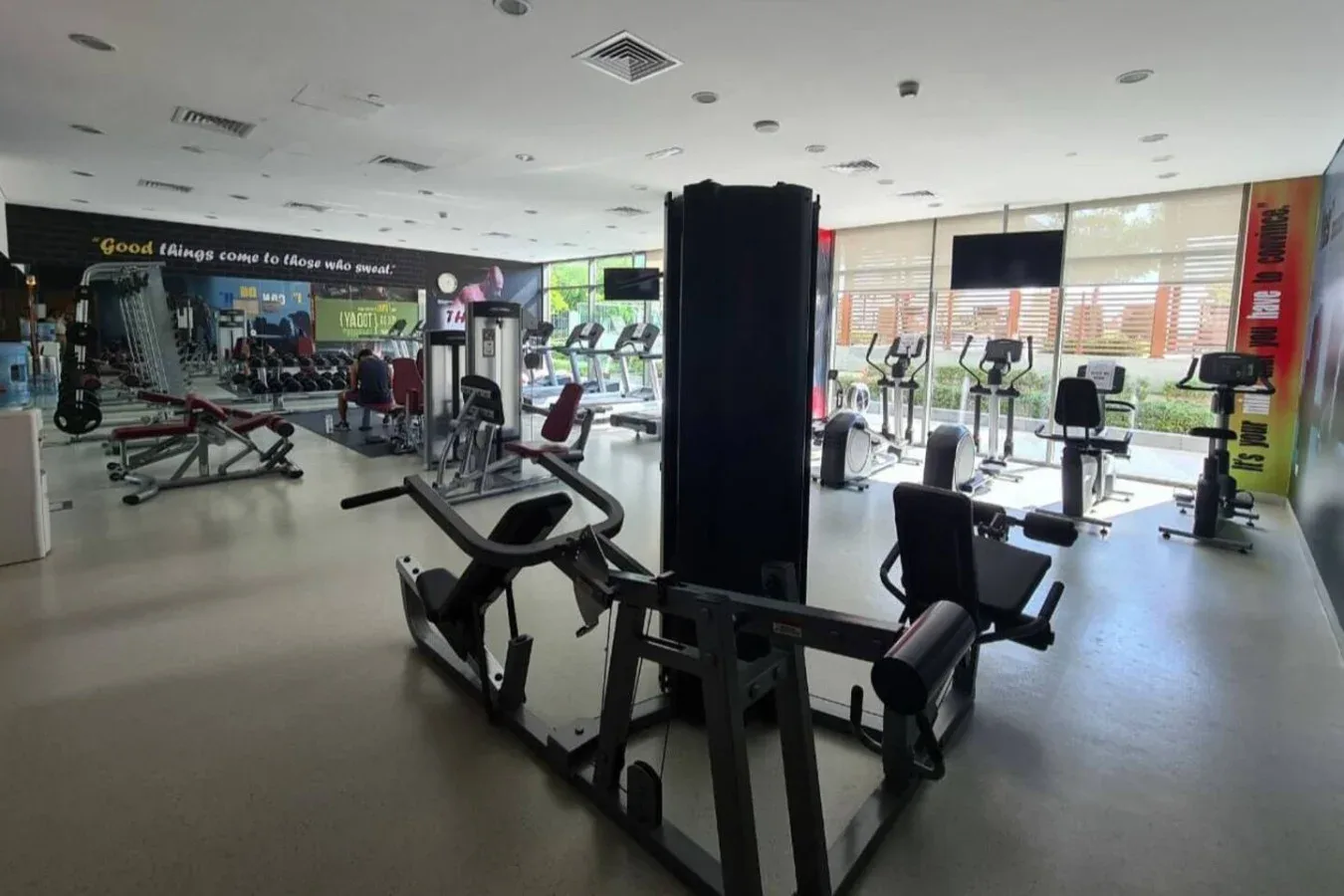 Un gimnasio con máquinas de ejercicio y ventanas grandes.