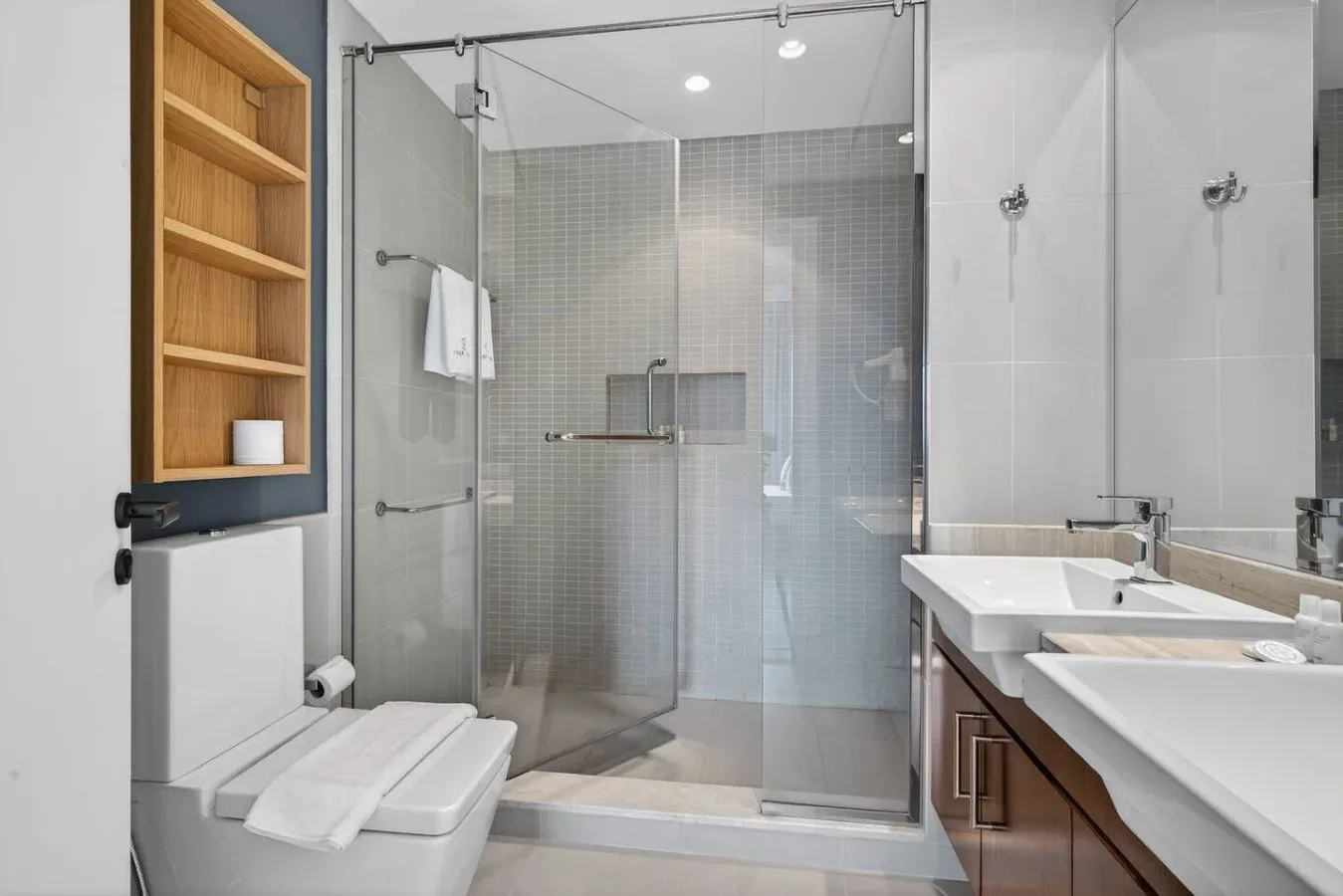 Un baño moderno con ducha de vidrio, inodoro y lavabo doble.
