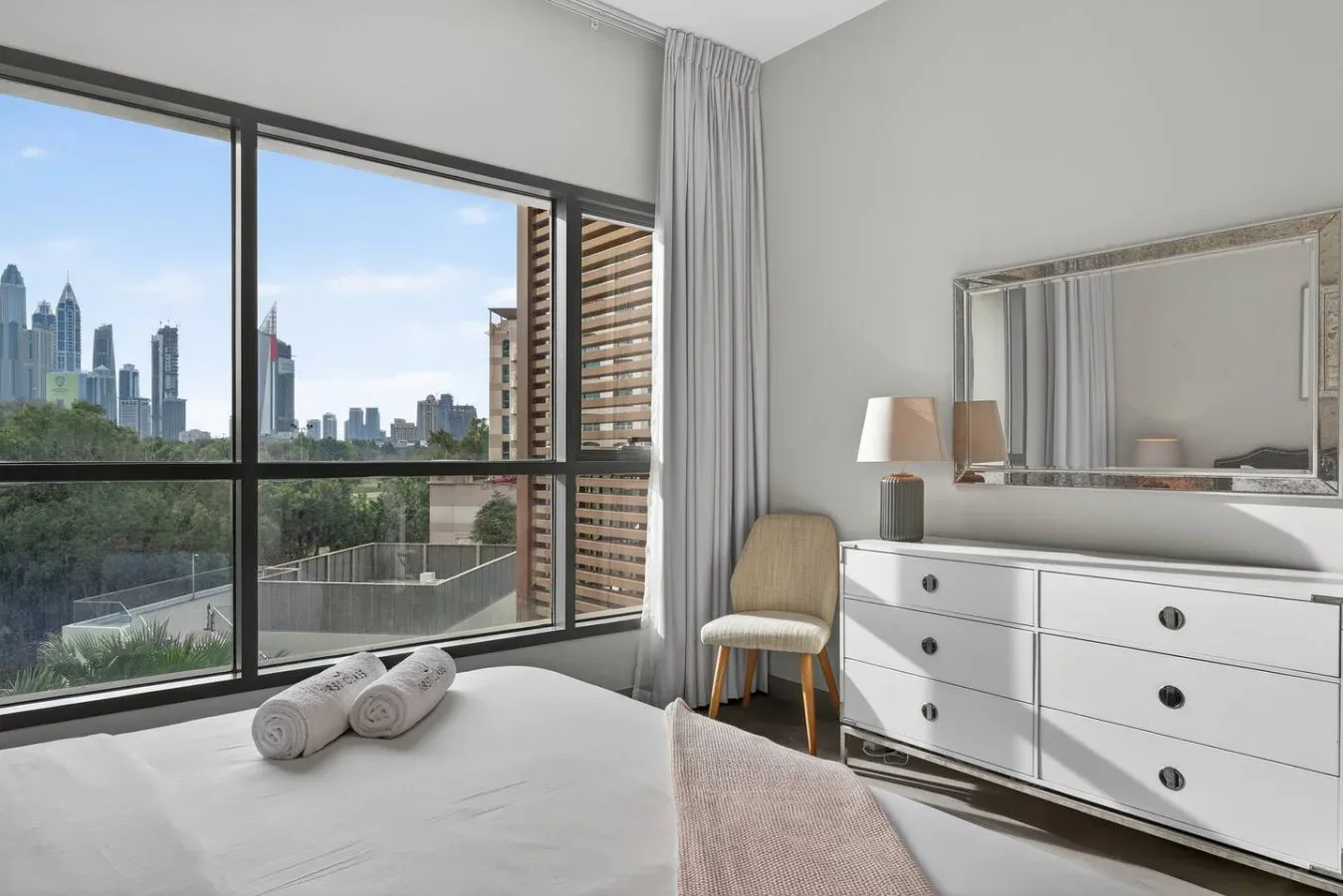 Un dormitorio luminoso con grandes ventanales que dan a la silueta de la ciudad.
