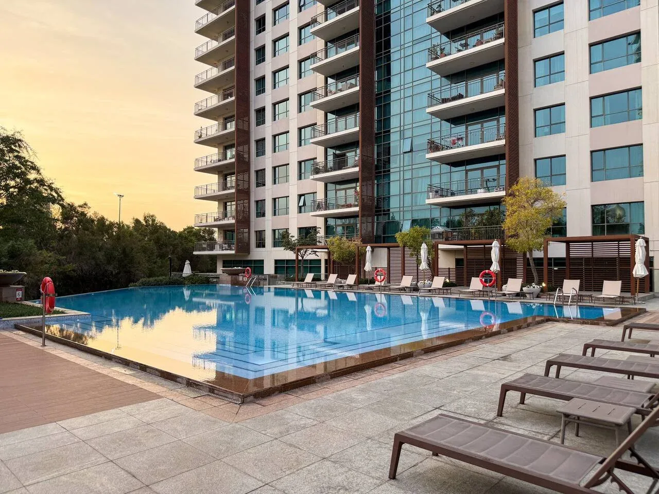 Una piscina al aire libre está junto a un edificio alto, con tumbonas alrededor.