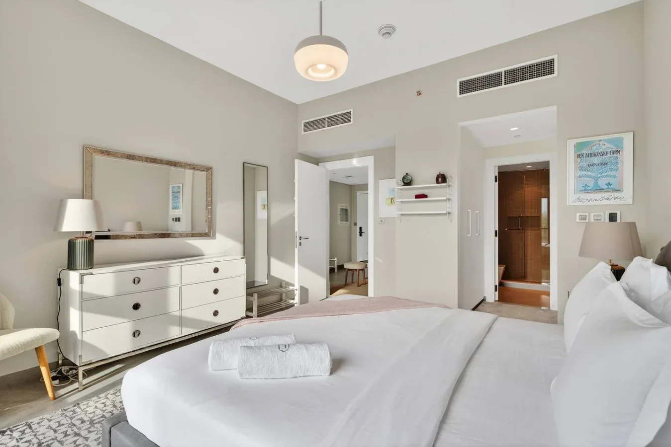 Un dormitorio con una cama bien arreglada, toallas dobladas y una cómoda.
