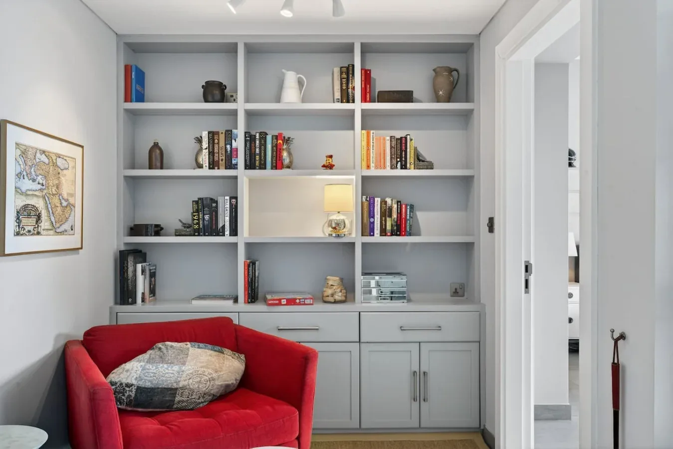 Una sala luminosa con estanterías empotradas y un asiento rojo.