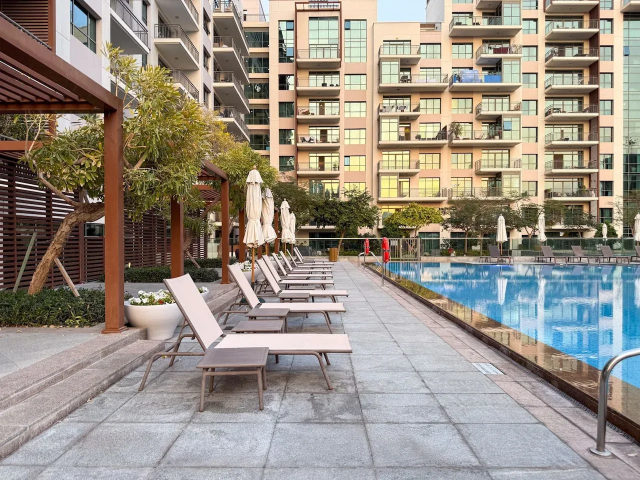 Una piscina al aire libre junto a una terraza pavimentada con asientos reclinables.