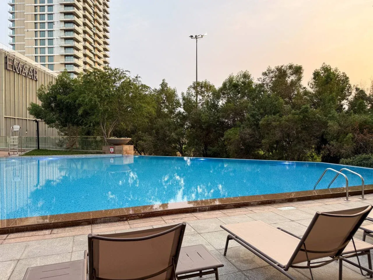 Una piscina al aire libre junto a una terraza pavimentada con tumbonas.