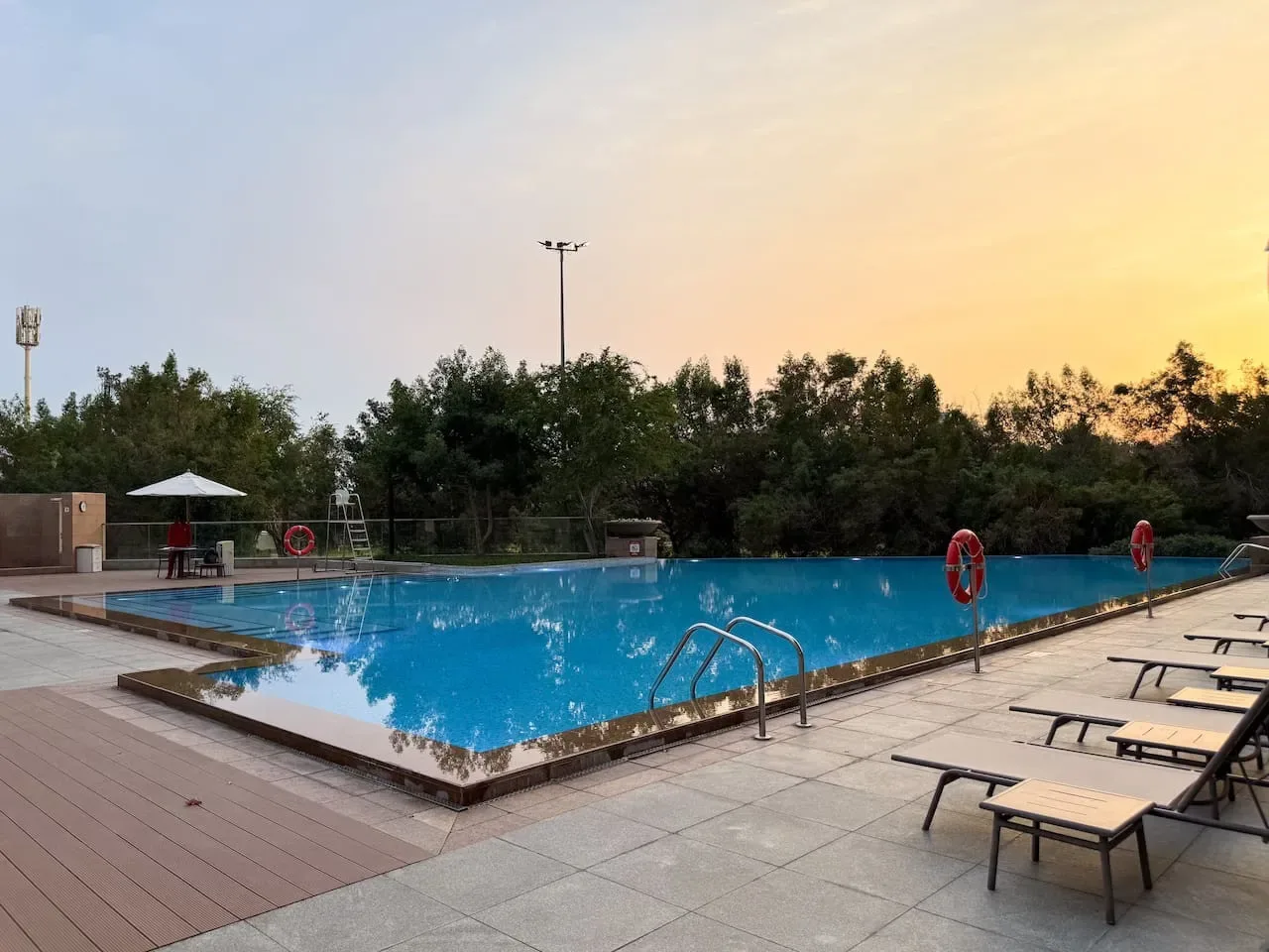 Una piscina al aire libre está rodeada de pavimento y tumbonas al atardecer.