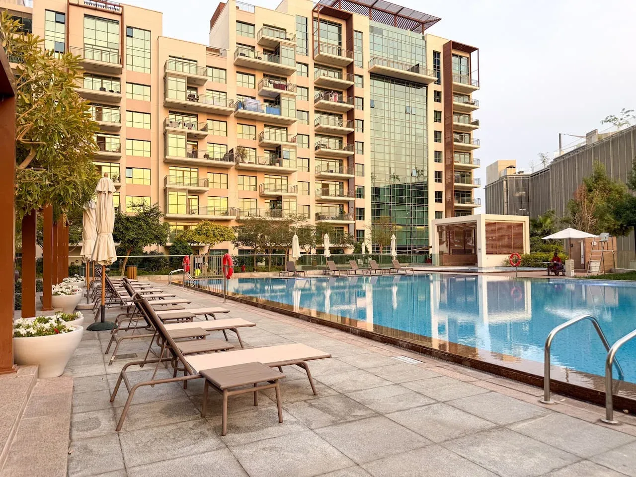 Una piscina y asientos de descanso están junto a un edificio residencial de varios pisos.