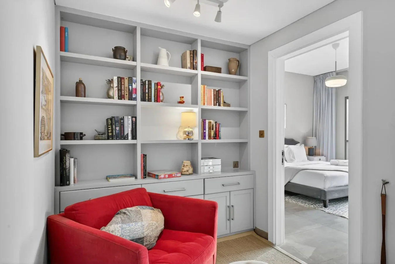 Una zona de asientos roja está frente a estantes empotrados, junto a la entrada abierta de un dormitorio.