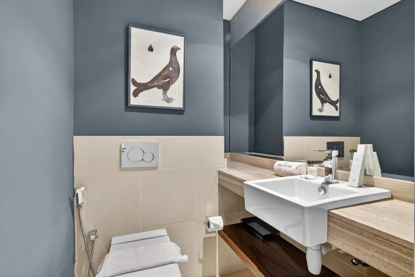 Un baño con lavabo blanco, inodoro y una lámina enmarcada de un pájaro.