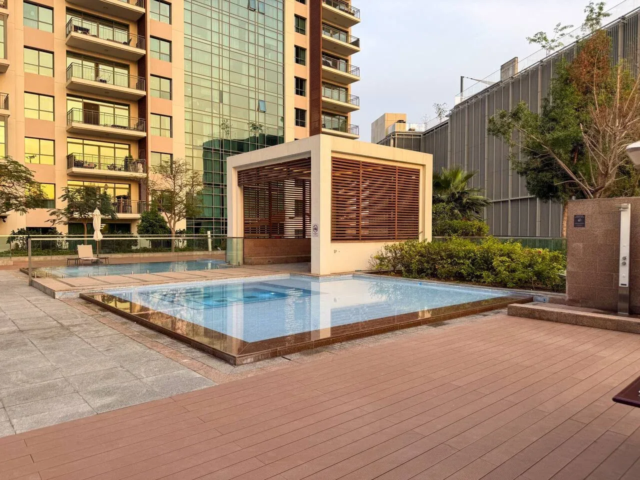 Una piscina al aire libre está junto a un pabellón sombreado y edificios de apartamentos.