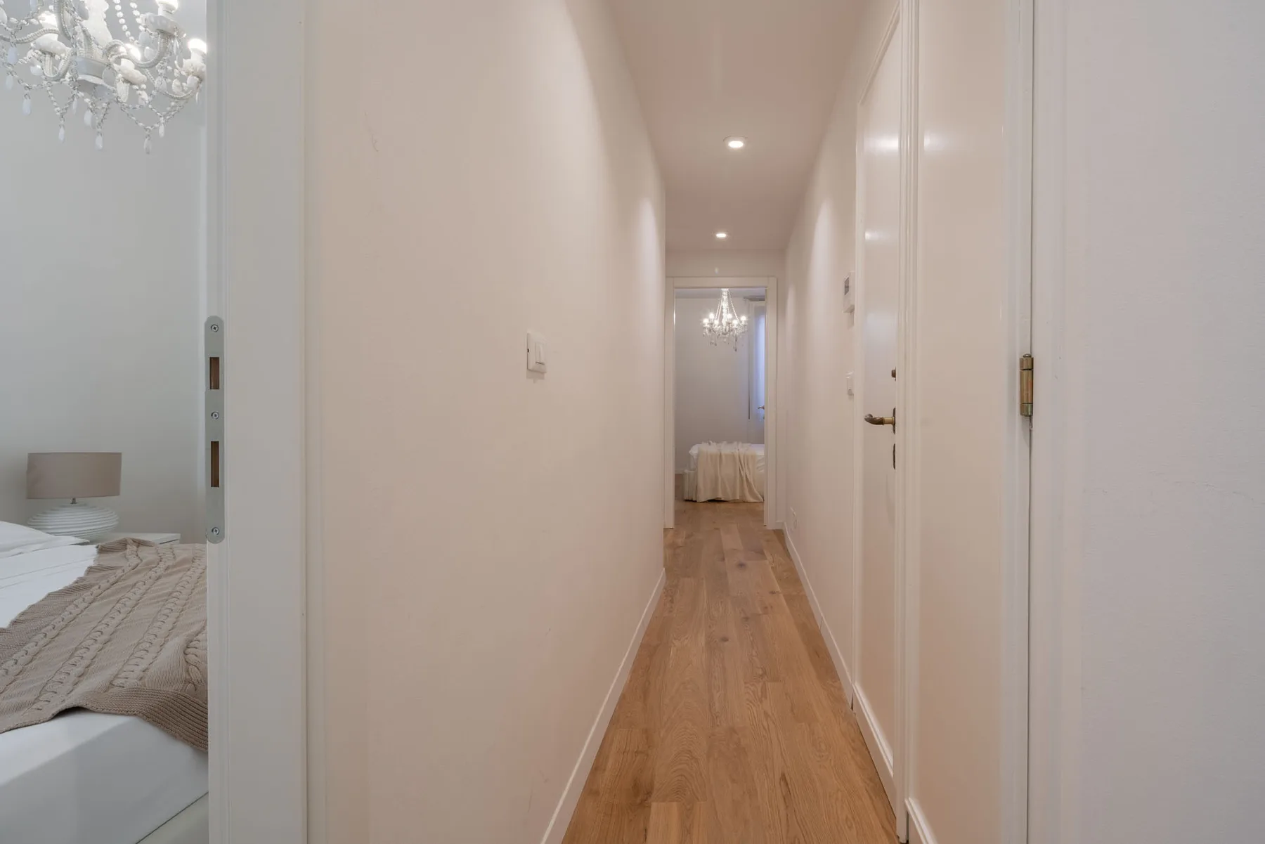 A hallway with wood flooring leads toward a bedroom at the far end.