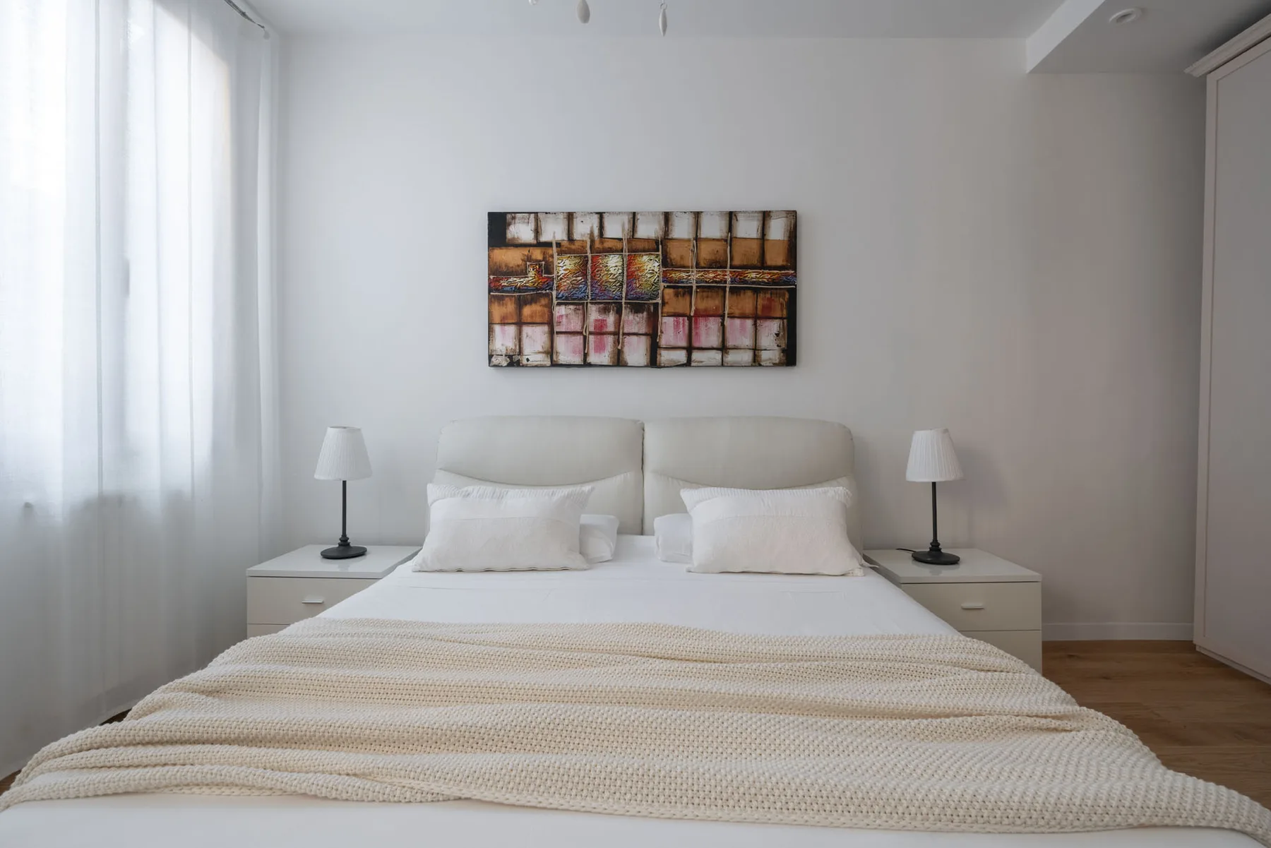 A bright bedroom with a neatly made bed and artwork above the headboard.