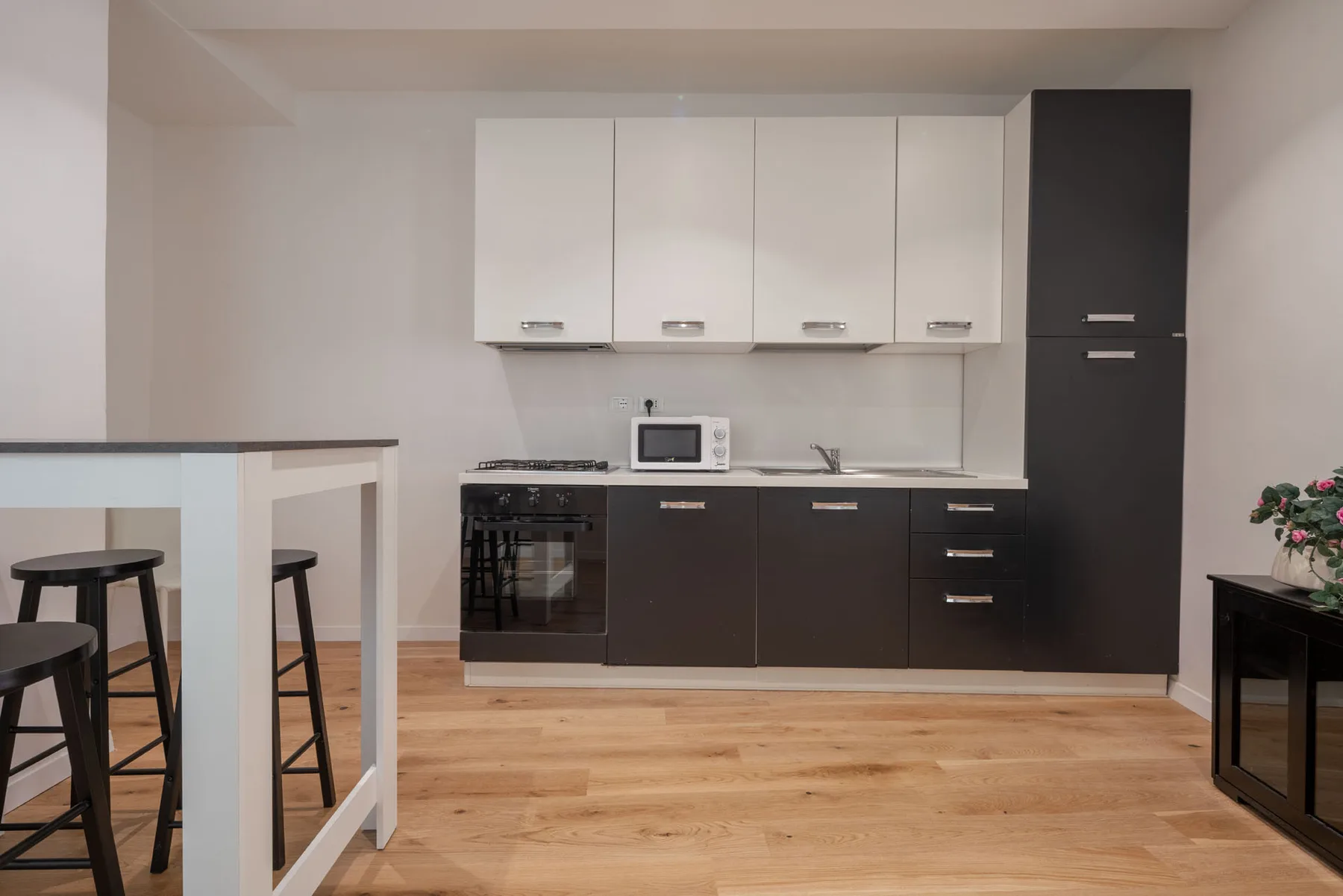 A modern kitchen with dark lower cabinets, white upper cabinets, and a wooden floor.