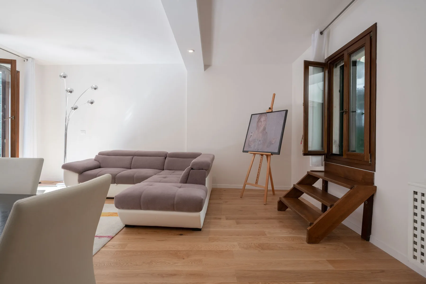 A bright living room with sectional seating and an easel beside the window.