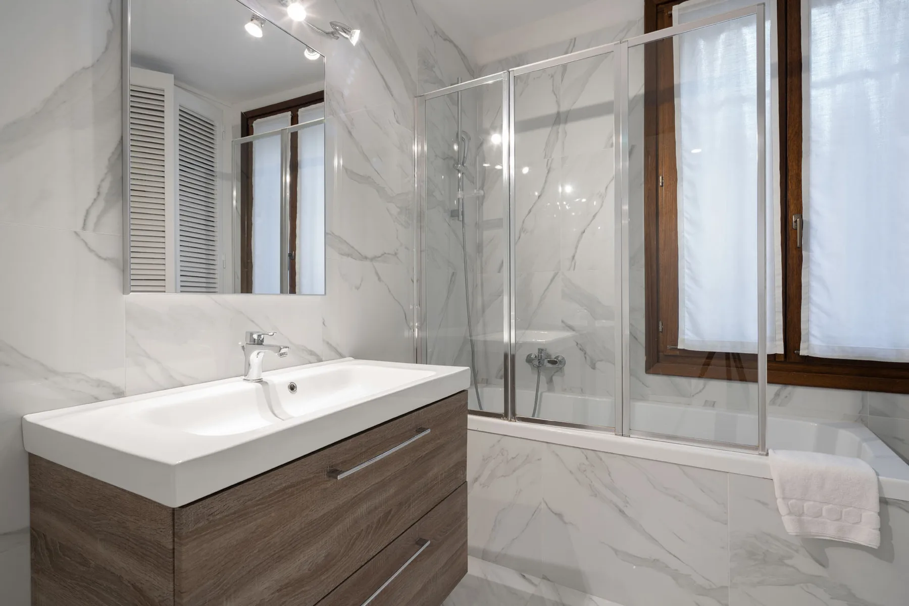 A bright bathroom with a vanity, mirror, and glass shower.
