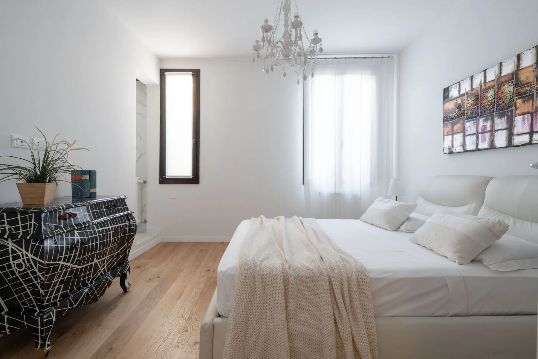 A bright bedroom with a large bed, a window, and a chandelier.