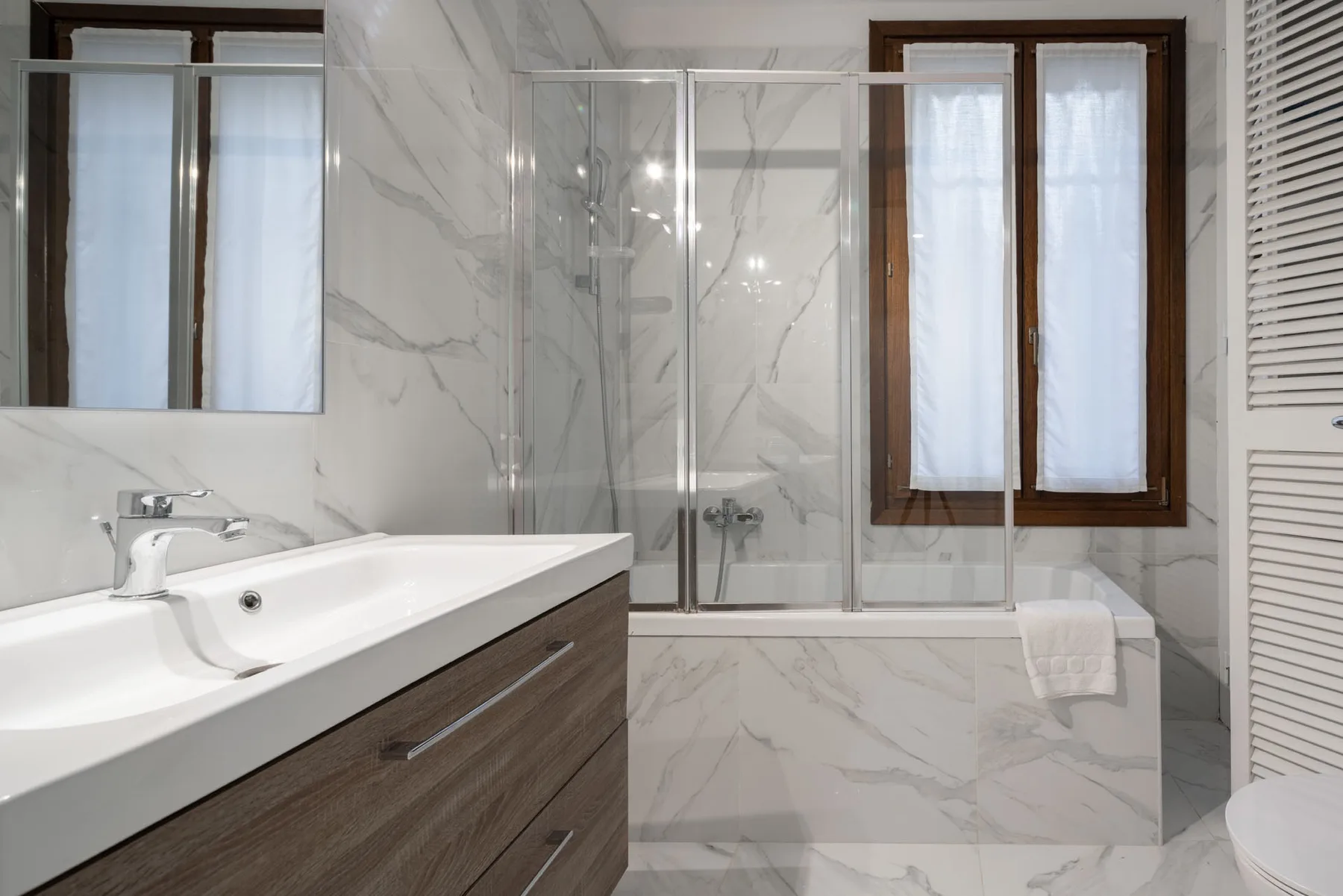 A bright bathroom with a glass shower, vanity, and windows.