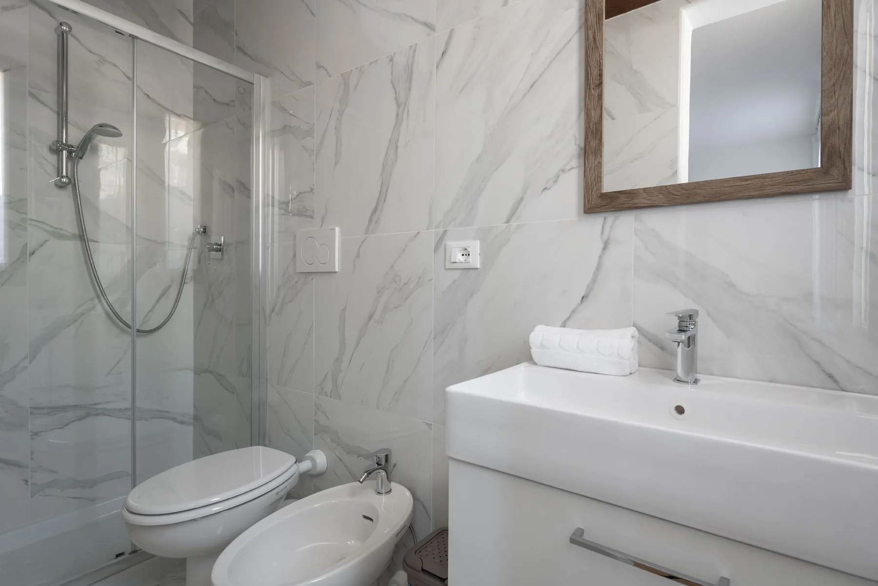 A bathroom with a glass shower, toilet, bidet, and sink.