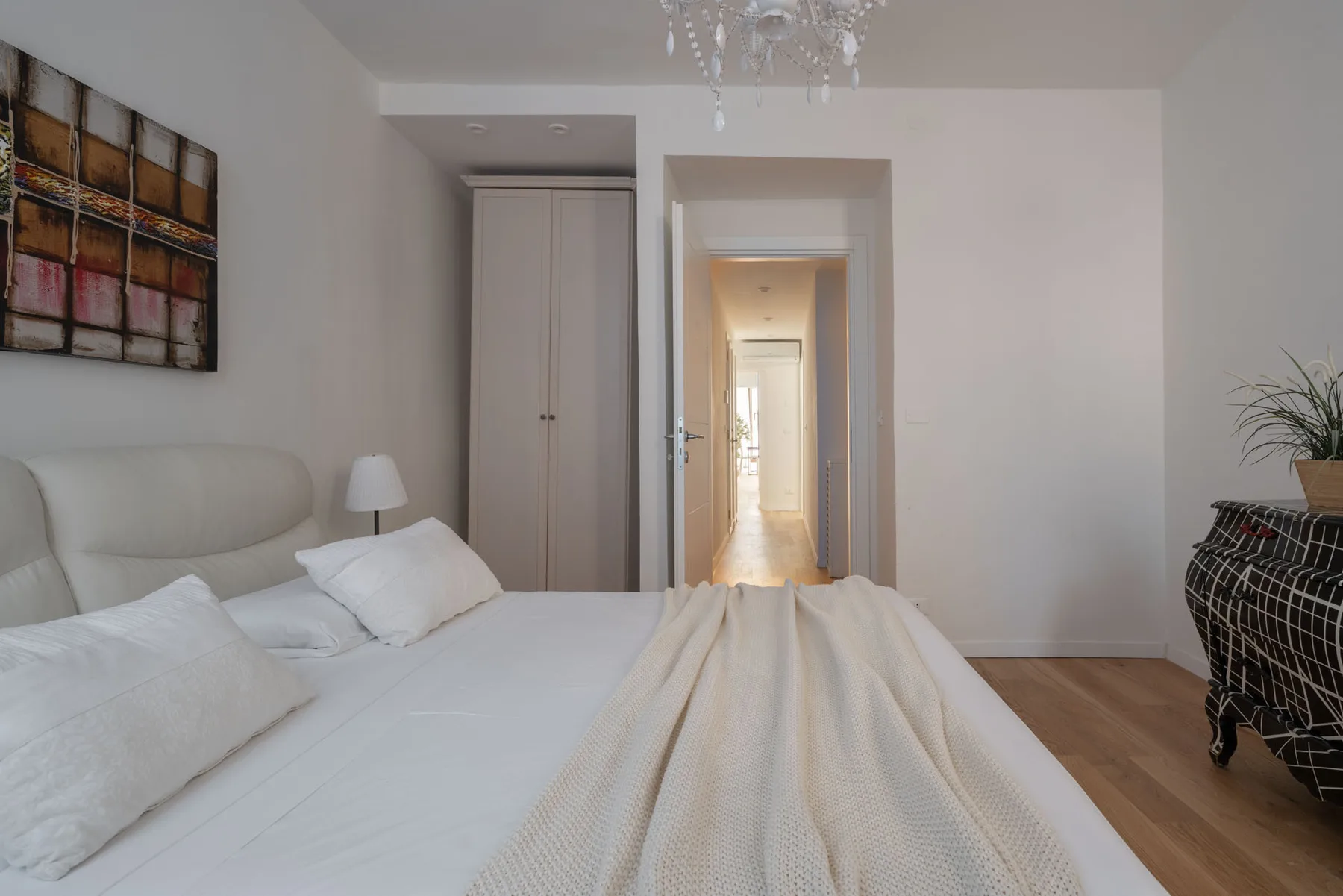 A bright bedroom with a bed, a wardrobe, and an open doorway.