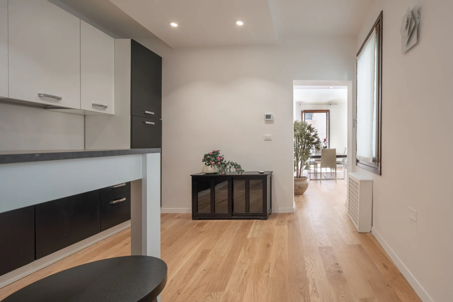 A bright kitchen and dining area with light wood flooring and a small cabinet.