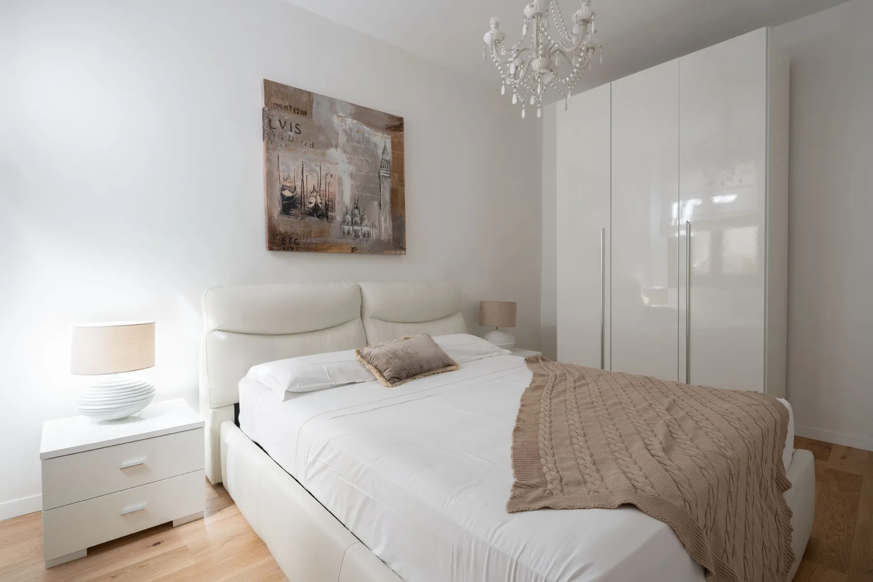 Un dormitorio luminoso con una cama blanca, una mesita de noche y un armario alto.