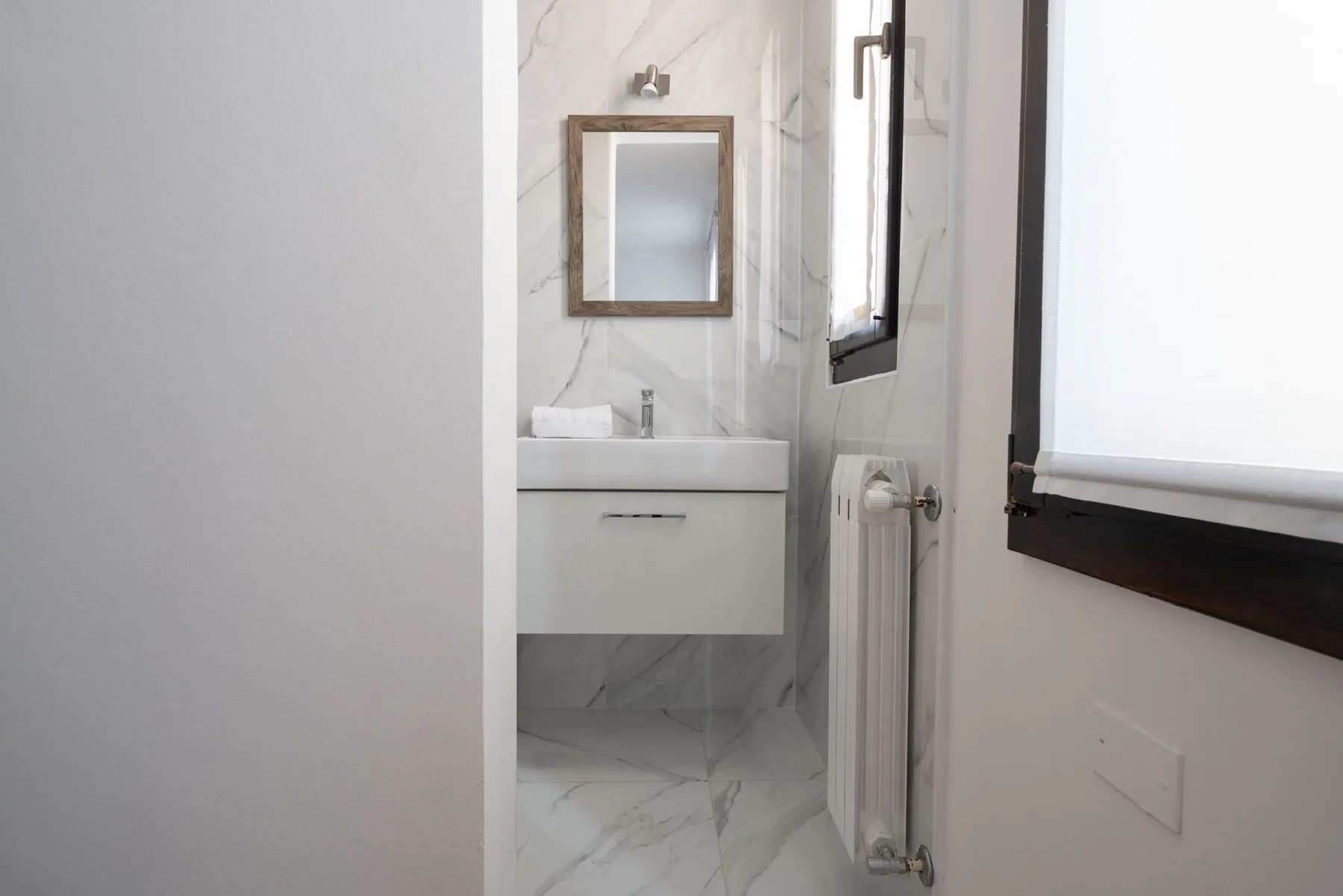 A compact bathroom with a sink, mirror, and radiator beside a window.