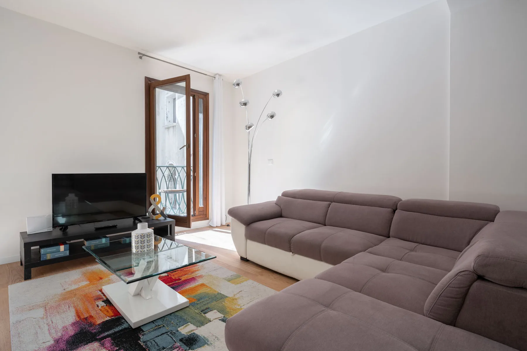 A living room with sectional seating, a television, and glass coffee tables.