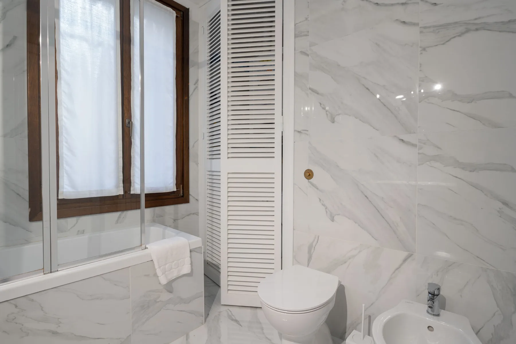 A bathroom with a toilet, bidet, and window beside a shower.