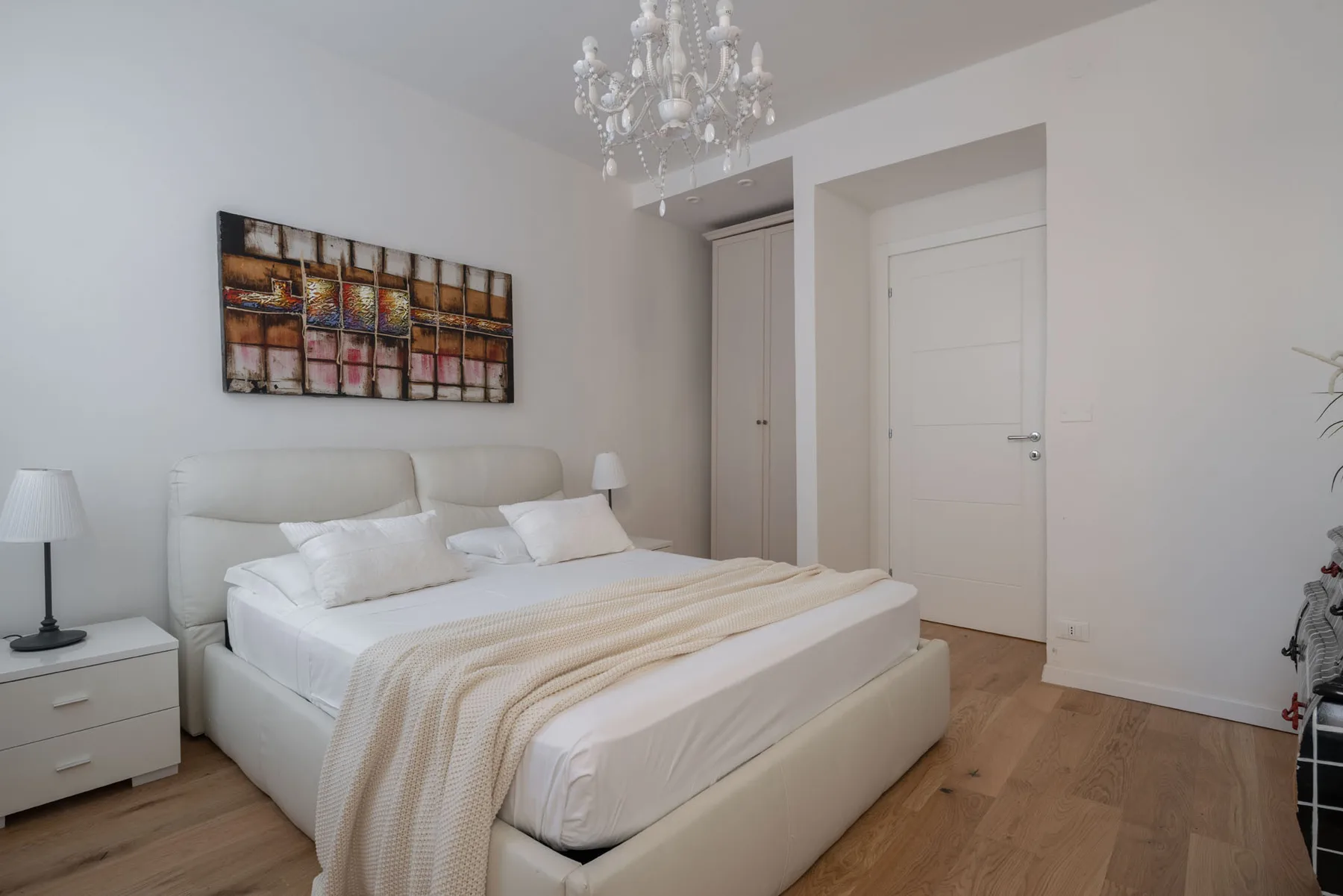 Un dormitorio con una cama tendida, mesitas de noche y cuadros en la pared.