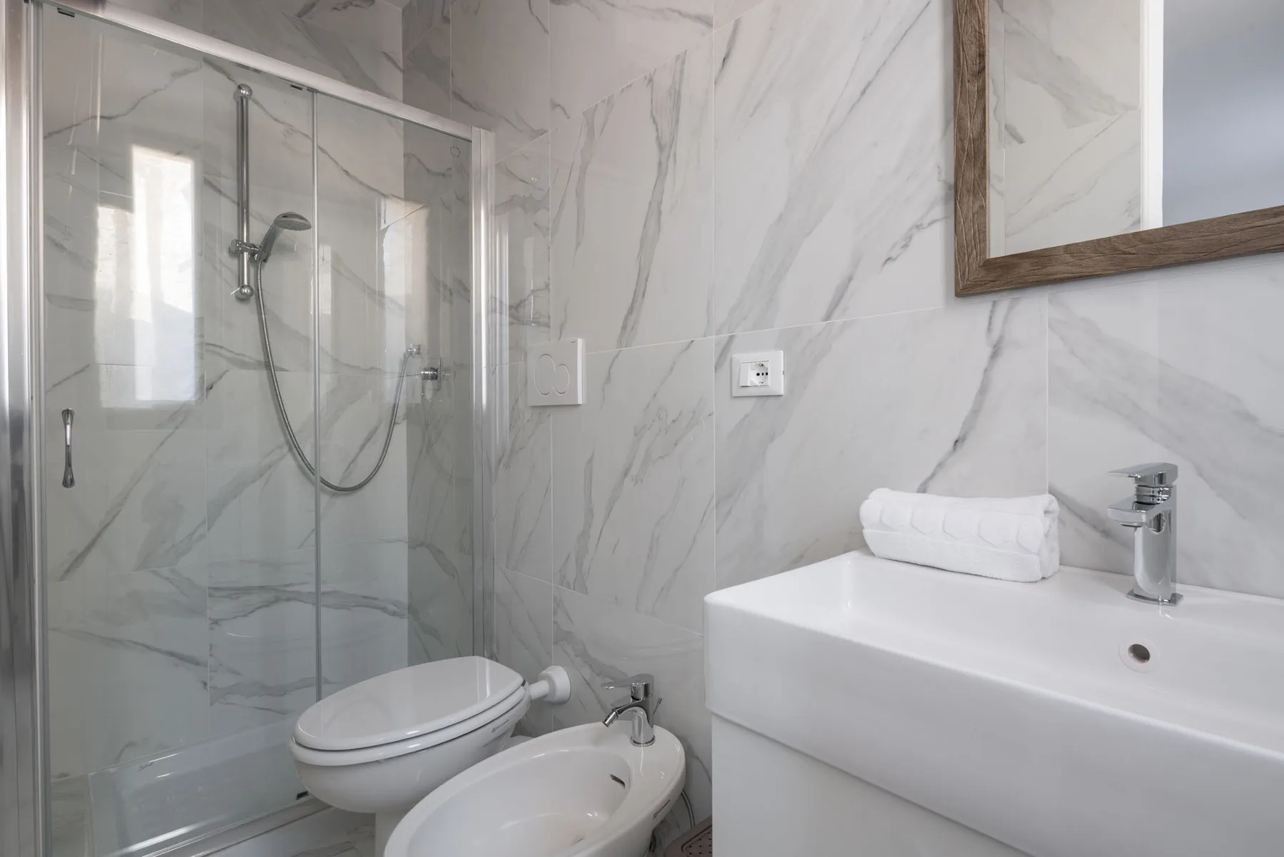 A bright bathroom with a glass shower, toilet, bidet, and white vanity.