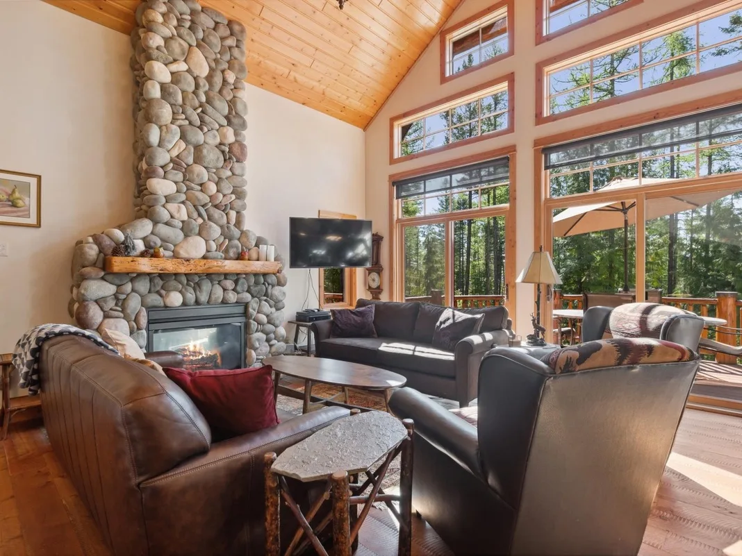 Una sala de estar con asientos alrededor de una chimenea de piedra y grandes ventanas.