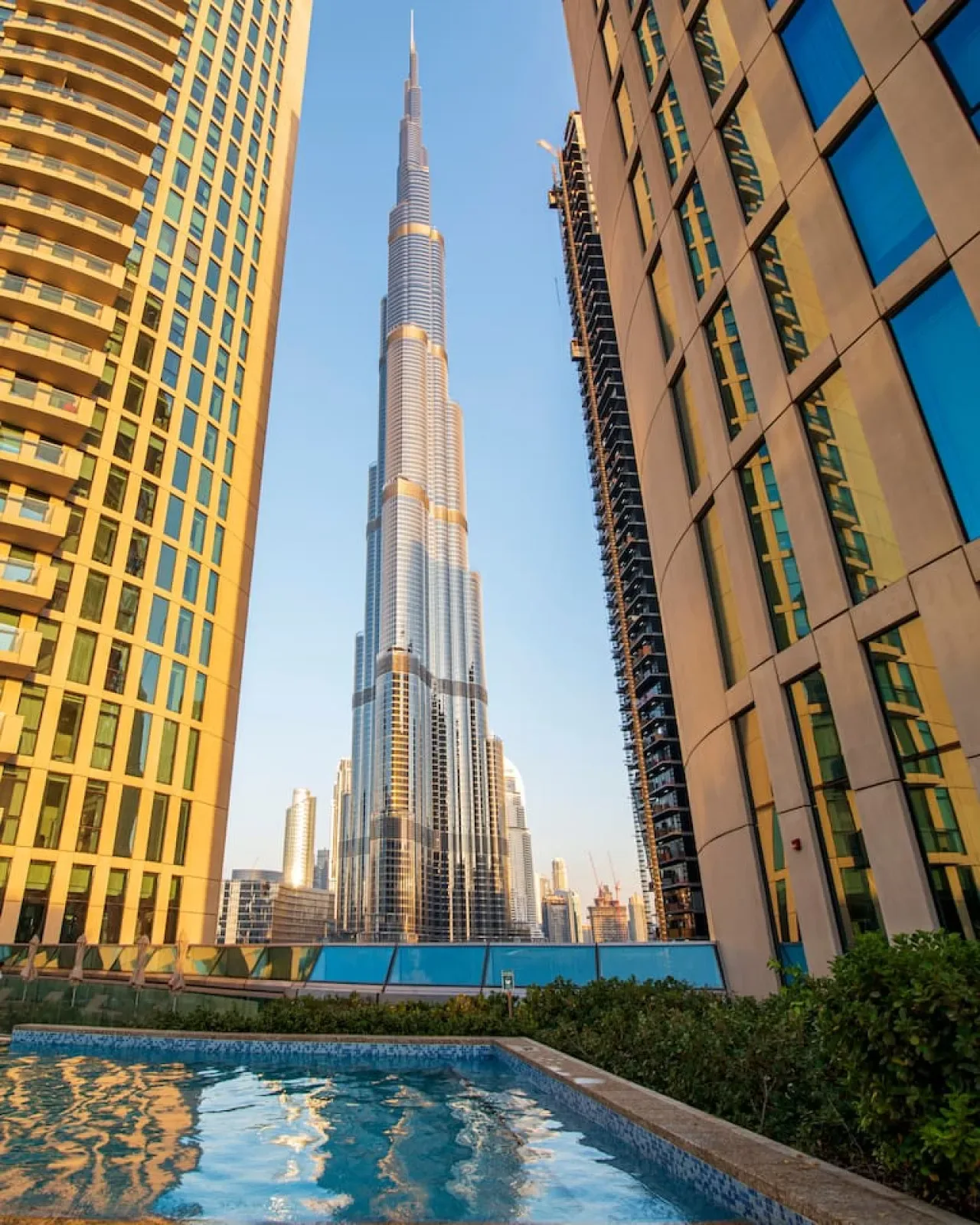 A cityscape frames a tall central skyscraper between neighboring towers, with a pool in the foreground.