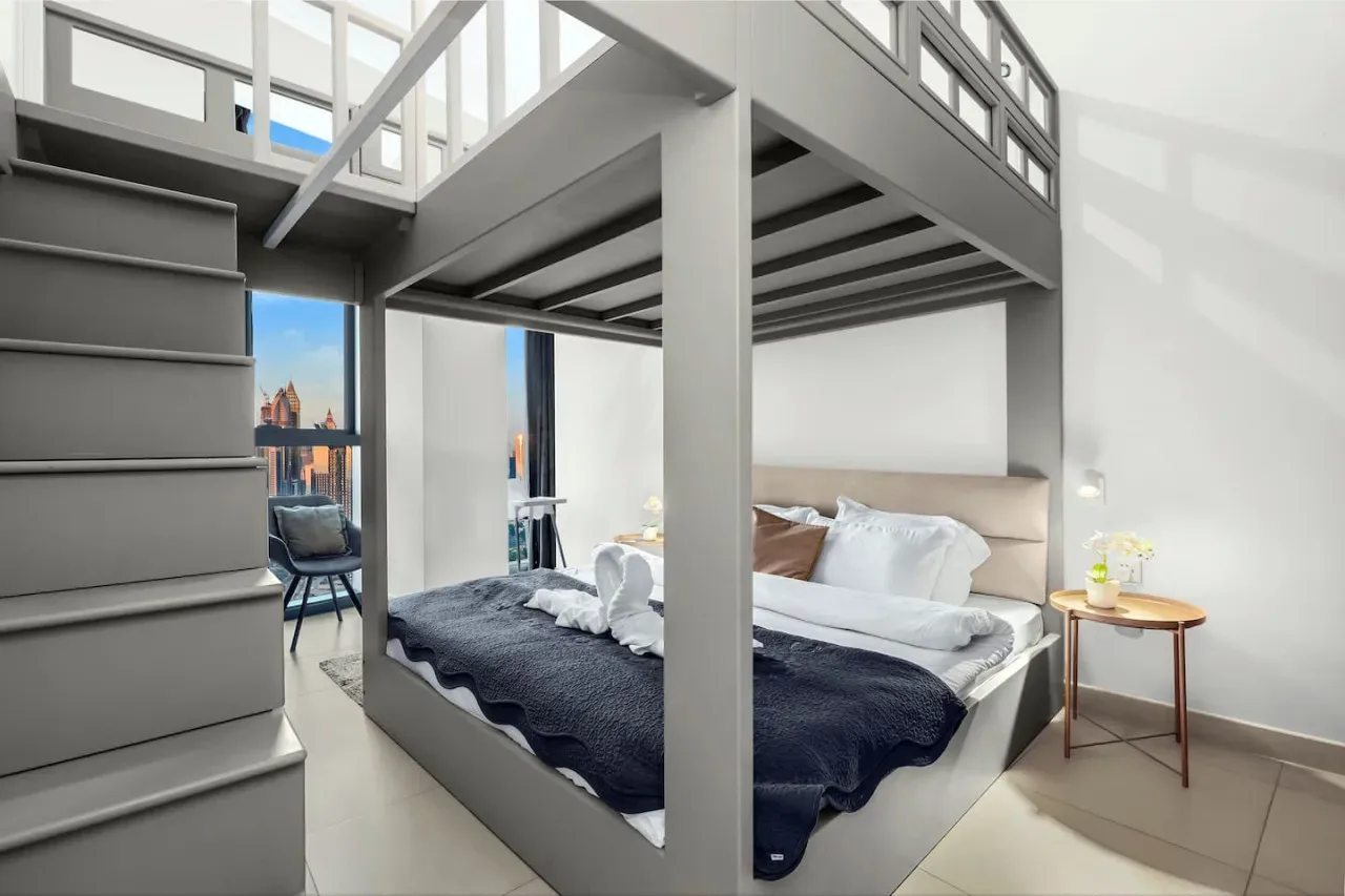 Un dormitorio luminoso con una cama debajo de una estructura elevada tipo altillo.