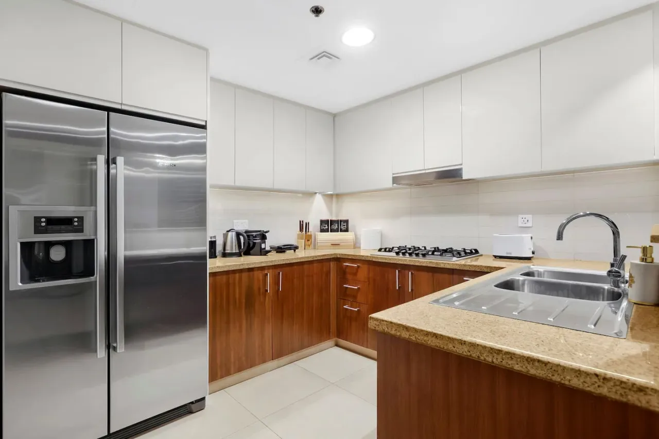 A bright kitchen with white cabinets, wood-toned lower cabinets, and stainless steel appliances.