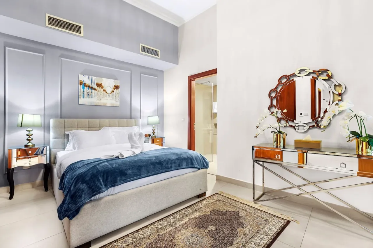 A bedroom with a bed, bedside tables, and a mirrored dresser.
