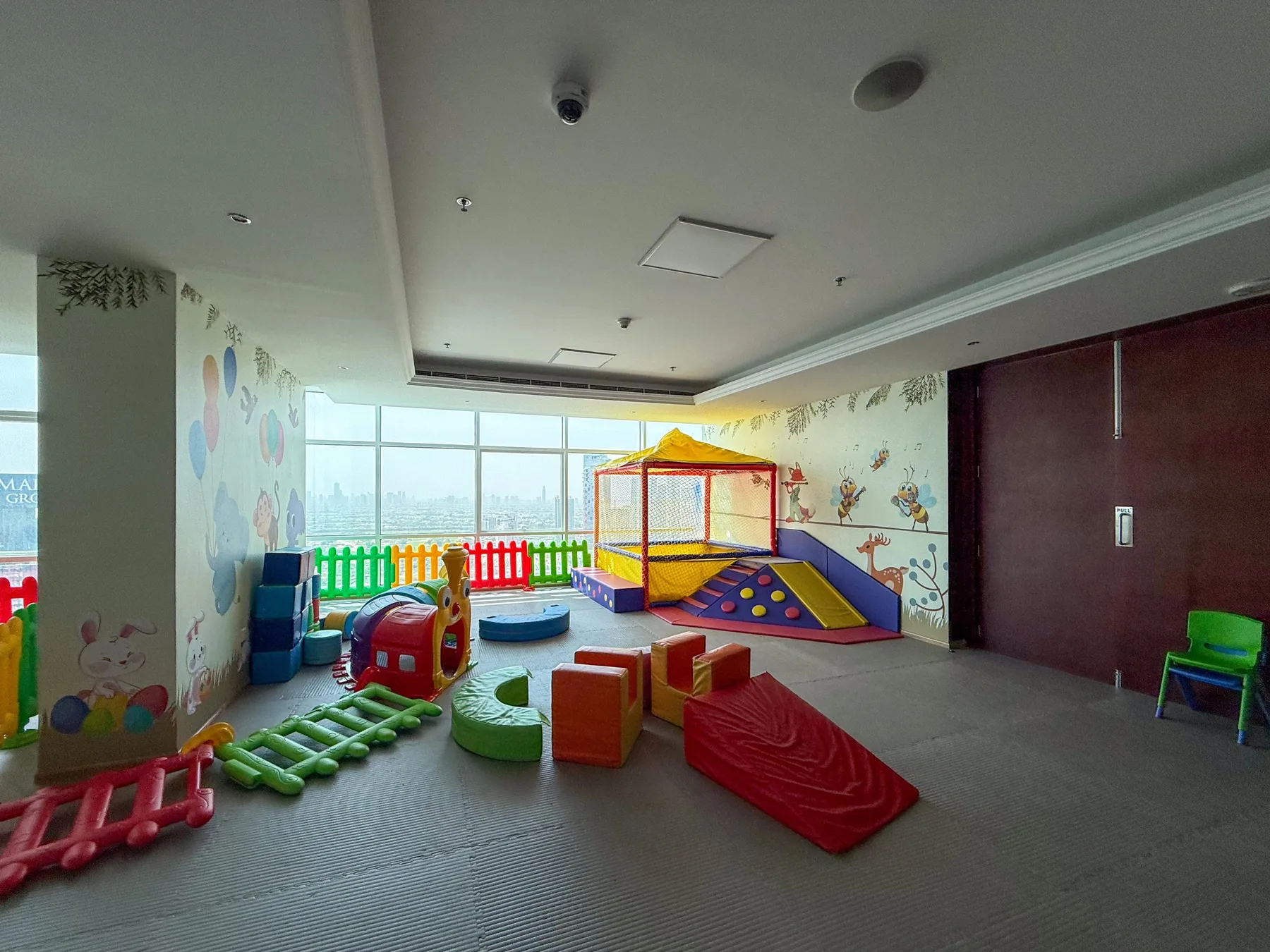 Una sala de juegos colorida con juegos blandos y grandes ventanales.
