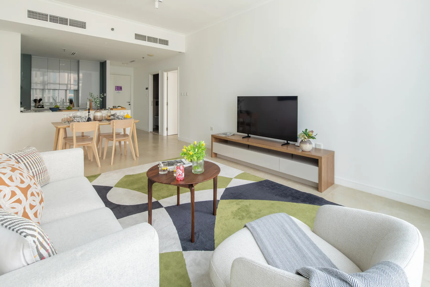 A bright living room with a television, seating, and an adjoining dining area.