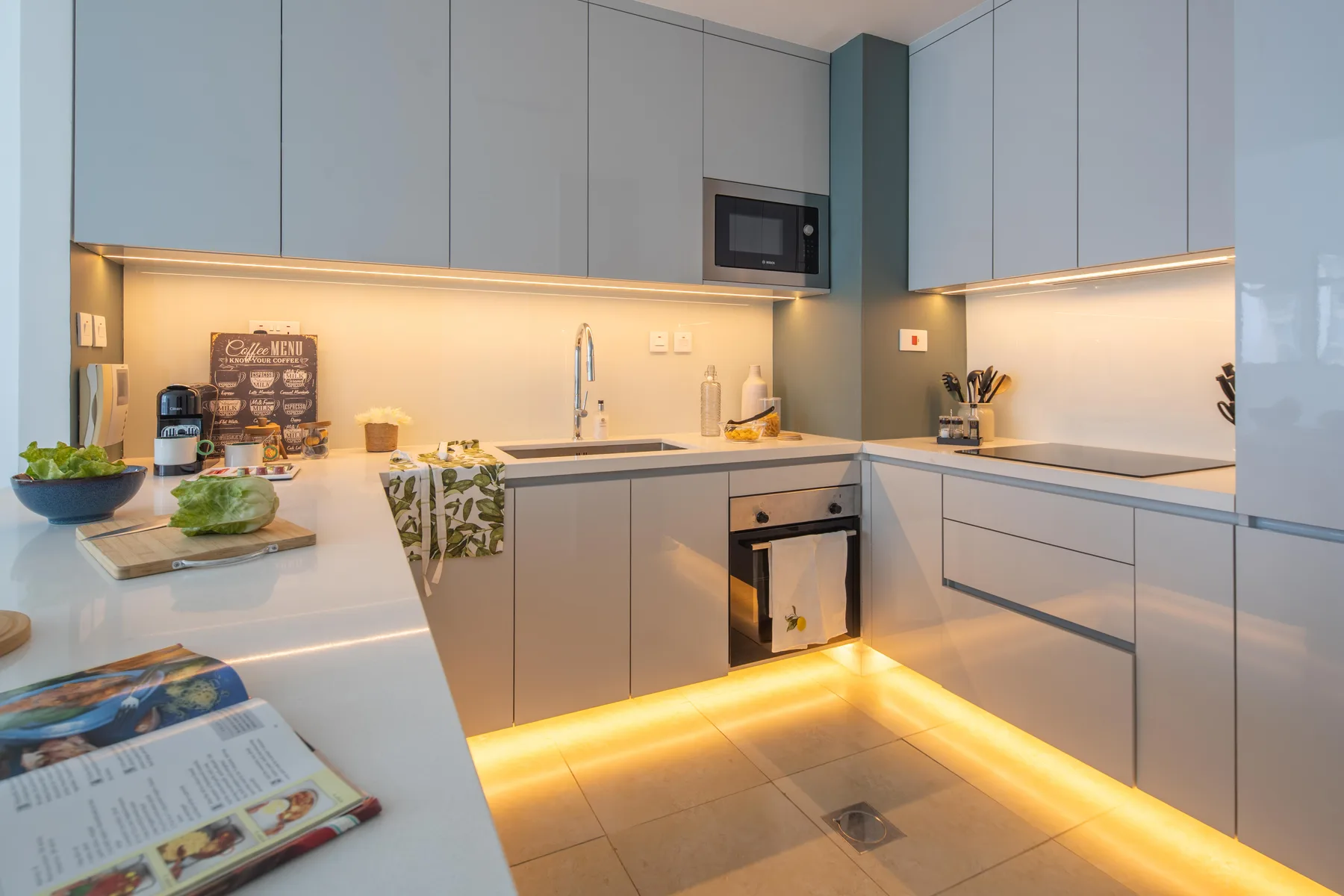 Una cocina moderna con gabinetes claros, encimeras e iluminación cálida bajo los muebles.